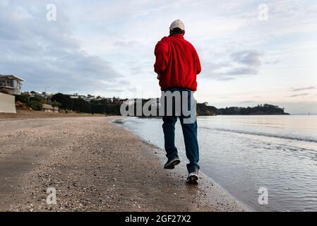 Mann, der am Strand von Milford bei Sonnenaufgang, North Shore, Auckland, läuft Stockfoto