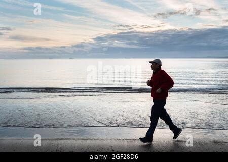 Mann, der bei Sonnenaufgang am Strand läuft Stockfoto