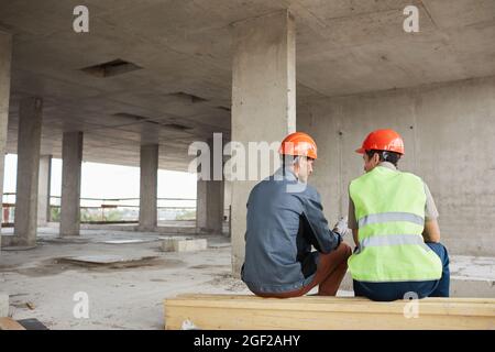 Rückansicht von zwei Bauarbeitern, die Harthüte tragen, während sie auf der Baustelle plaudern, Platz kopieren Stockfoto