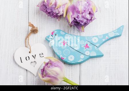 Blauer HolzVogel mit violetten Tulpen und weißem Herz. Stil romantisch, schäbig chic, Provence. Hochzeit, Verlobung, Datum. Stockfoto