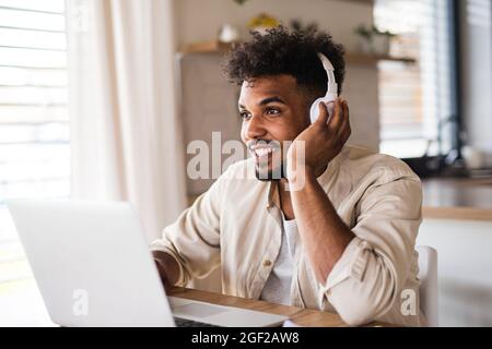 Junger Student mit Laptop und Kopfhörern zuhause, studieren. Stockfoto