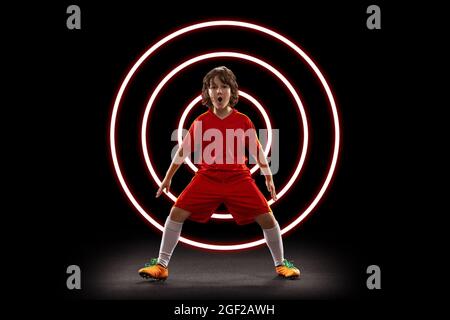 Abstraktes Design, Konzept des Sports, Action, Bewegung im Sport. Junger kleiner Sportler, Fußballspieler in Neonlicht auf schwarzem Hintergrund Stockfoto