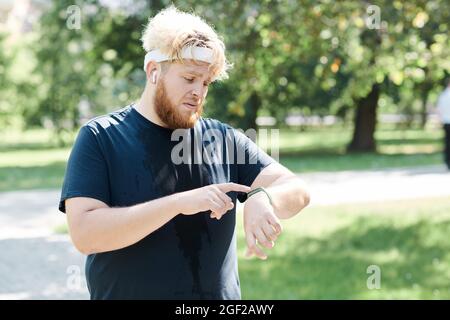 Übergewichtiger Mann mit Fitness-Tracker an der Hand beim Joggen im Park im Freien Stockfoto