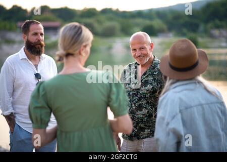 Reifes Paar mit älteren Eltern auf Spaziergang am See im Sommerurlaub, reden. Stockfoto