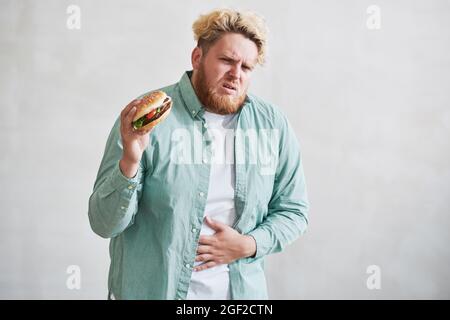 Übergewichtiger Mann mit Bauchschmerzen durch den Verzehr von Fast Food vor dem weißen Hintergrund Stockfoto