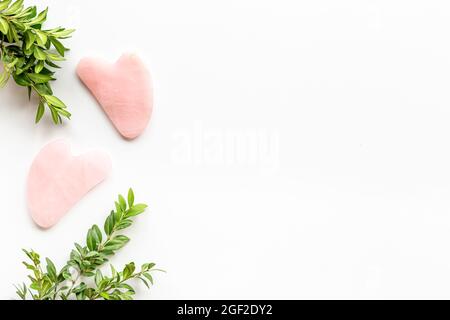 Rosenquarz Gua Sha Massagestein mit grünen Blättern Stockfoto