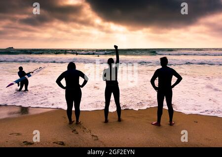 Mitglieder des Newquay Surf Lifesaving Club bei einem Training am Fistral Beach, der von der untergehenden Sonne in Newquay in Cornwall umrastet wird. Stockfoto