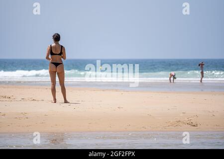 Rückansicht einer jungen Frau in einem Bikini, die am Strand steht und das Meer bewundert Stockfoto