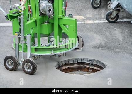 Auf der Straße wird eine Schachtabdeckung mit einer Spezialmaschine gefräst, Kanalisationsarbeiten, Kanalarbeiten, Kanalarbeiten, Straßenbau Stockfoto