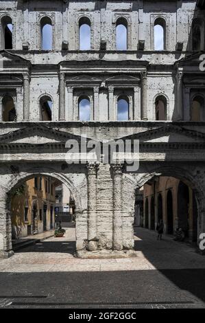 Der Haupteingang zum antiken römischen Verona in Venetien, Italien, die Porta Borsari, wurde im 1. Jahrhundert n. Chr. als Porta Iovia nach einem nahe gelegenen Jupiter-Tempel erbaut. Der heutige Name erinnert an die bursarii, mittelalterliche Steuereinnehmer, die ‘„Bursa“-Ledertaschen verwenden, um Zölle auf Waren zu erheben, die in die Stadt ein- oder ausreisen. Unter geriffelten korinthischen Säulen, Giebeln und Bogenfenstern erzählen lateinische Inschriften von seinem Wiederaufbau im Jahr 265 n. Chr. Die weiße Kalksteinfassade überspannt nun den verkehrsfreien Corso Porta Borsari, am Anfang der römischen Straße Via Postumia, die Verona mit Genua und Triest verbindet. Stockfoto