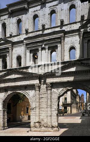 Die Porta Borsari, der wichtigste antike römische Eingang nach Verona, Venetien, Italien. Das Tor wurde als quadratische Festung mit flankierenden Türmen im 1. Jahrhundert n. Chr. als Porta Iovia nach einem Jupitertempel erbaut. Der heutige Name leitet sich von den Bursarii ab, mittelalterlichen Steuereintreibern, die ‘„Bursa“-Geldbörsen verwenden, um Zollgebühren für Waren zu erheben, die in die oder aus der Stadt einreisen. Inmitten von geriffelten Säulen, Giebeln und Bogenfenstern dokumentieren lateinische Inschriften den Wiederaufbau des Tores im Jahr 265 n. Chr. Die weiße Kalksteinfassade überspannt den verkehrsfreien Corso Porta Borsari, den Beginn der Via Postumia Roman Road. Stockfoto