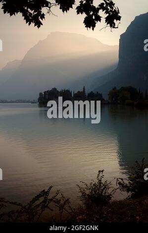 Sonnenuntergang auf einem alpinen See in Norditalien, dem Lago di Toblino in Trentino-Südtirol. In der Silhouette sehen Sie eine mittelalterliche Burg, das Castel Toblino, gegründet in den 1100s Jahren und einst eine begehrenswerte Sommerresidenz für die mächtigen Prinzbischöfe von Trent. Stockfoto