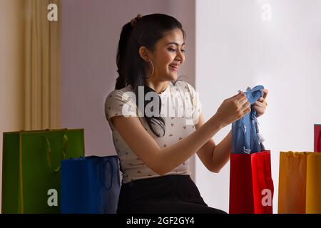 Eine junge Frau sitzt inmitten farbenfroher Einkaufstaschen und packt ihr neues Kleid aus. Stockfoto