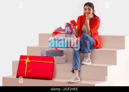 Eine junge Frau, die auf einer Treppe mit Geschenkschachteln in der Hand und daneben sitzt. Stockfoto