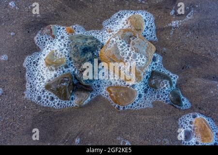 Kieselsteine und Meeresschaum am Strand von Marske-by-the-Sea, North yorkshire, großbritannien Stockfoto