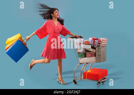 Eine junge Frau, die bunte Einkaufstaschen trägt und einen Wagen voller Geschenkkartons bewegt. Stockfoto