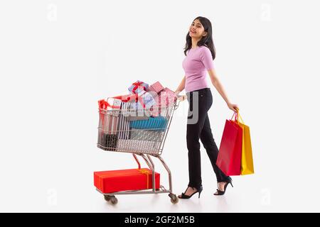 Porträt einer jungen Frau, die Einkaufstaschen trägt und einen Wagen voller Geschenkboxen bewegt. Stockfoto