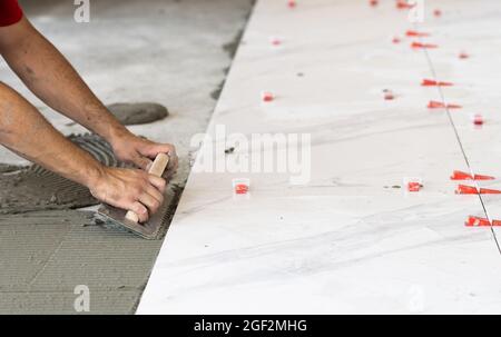 Festlegung von Keramikfliesen. Troweling Mörtel auf Betonboden in der Vorbereitung für die Verlegung von weißen Bodenfliesen. Stockfoto