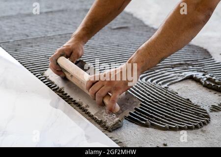 Festlegung von Keramikfliesen. Troweling Mörtel auf Betonboden in der Vorbereitung für die Verlegung von weißen Bodenfliesen. Stockfoto