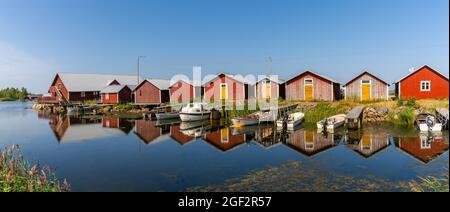 Svedjehamm, Finnland - 28. Juli 2021: Panoramablick auf bunte Fischerhütten und Boote, die sich im Wasser unter blauem Himmel spiegeln Stockfoto