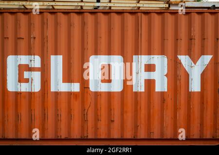 Das Wort Glory auf einem Industriebehälter in weißem Emaille auf orangefarbenem Hintergrund geschrieben Stockfoto