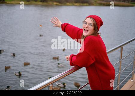 Frau, die Enten im Herbstpark in der Nähe des Wasserteiches füttert Stockfoto