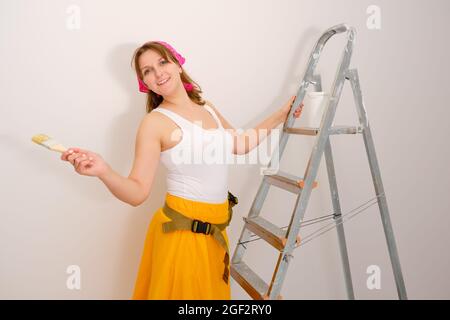 Frau Maler slawische Erscheinung steht neben der Leiter auf dem Hintergrund einer weißen Wand Stockfoto