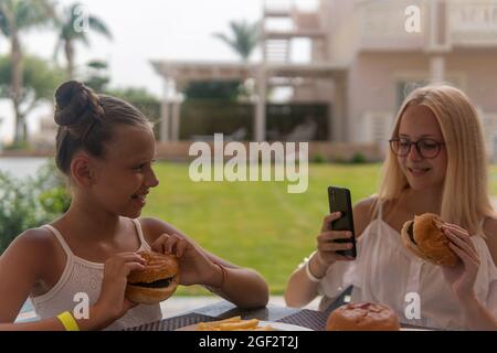 Zwei Mädchen im Teenageralter essen Fast Food und fotografieren Stockfoto