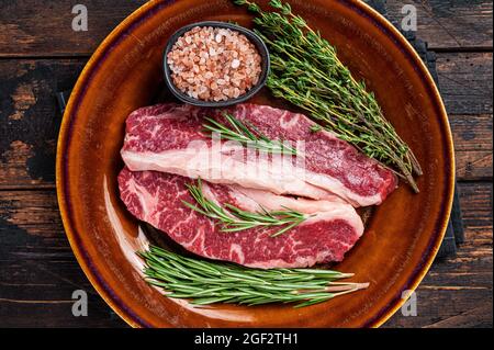 Zwei Raw Striploin-Steaks in Scheiben oder New York-Steaks, Rinderfleisch. Dunkler Holzhintergrund. Draufsicht Stockfoto