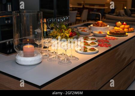 Vorbereitung auf das Weihnachtsbankett. Weingläser, Snacks auf dem modernen Küchentisch stehen bereit zum Servieren. Abendlicht und Kerzen. Silvester. Stockfoto