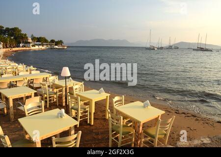 Tische zum Abendessen am Strand bei Sonnenuntergang über dem Meer in Aegina in Griechenland Stockfoto