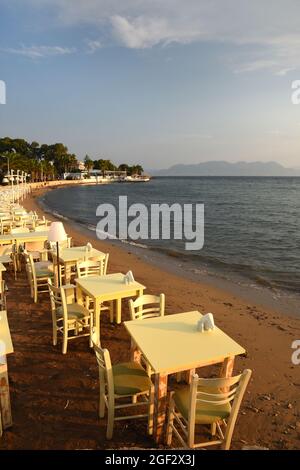 Tische zum Abendessen am Strand bei Sonnenuntergang über dem Meer in Aegina in Griechenland Stockfoto