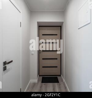 Modernes Interieur der modernen Wohnung. Vorderansicht der Eingangstür. Weiße Wände. Parkettfußboden. Stockfoto