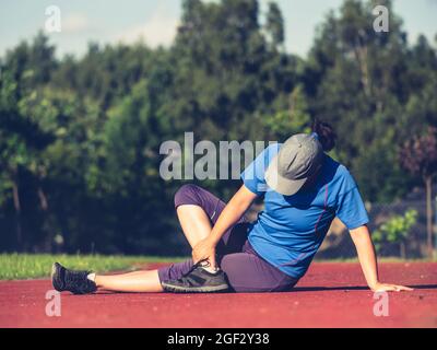 Eine Läuferin übt Yoga und dehnt den Körper vom Rücken bis zum Beinkrampf im Stadion Stockfoto