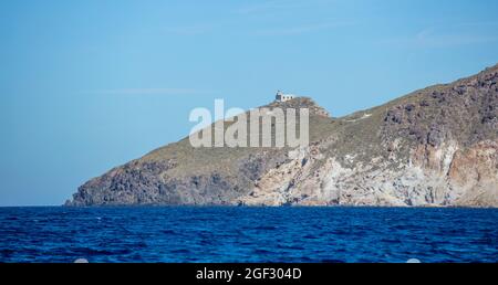 Kimolos Insel, Kykladen Griechenland. Blau türkisfarbene Wellen Ägäis felsigen Hügel mit Gebäude auf der Oberseite, klaren Himmel Hintergrund. Reiseziel Sommer Kreuzfahrt Bucht Stockfoto