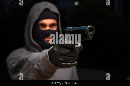 Killer mit Balaclava, mit einer Waffe in der Hand, bewaffnet Raub Konzept. Mann, der mit einer Pistole anvisierte, dunkler Hintergrund, Nahaufnahme. Stockfoto