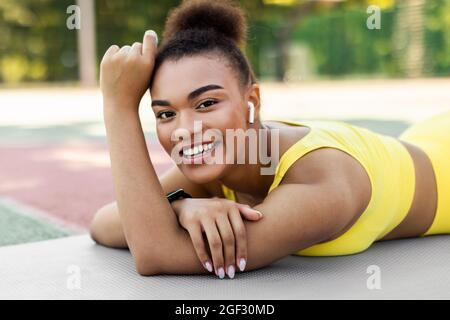 Sportliche schwarze Frau in gelber Sportkleidung liegend und posiert Stockfoto