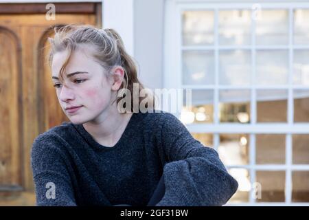 Ein Teenager-Mädchen, das allein draußen sitzt und gelangweilt aussieht. Stockfoto