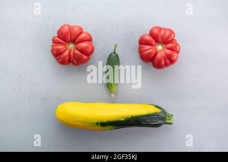 Lustige Gesichtsform von pflanzlichen Produkten gebildet: Tomaten, Gurke, Zucchini, Draufsicht Hintergrund. Ausgewogene gesunde Ernährung Kochen Zutaten. Gesund f Stockfoto