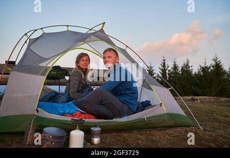 Mann und Frau sind nach einer süßen Nacht unter freiem Himmel im Zelt aufgewacht und haben dabei den atemberaubenden Blick auf die morgendlichen Berge beobachtet. Konzept von Wandern, Camping und Beziehungen. Stockfoto