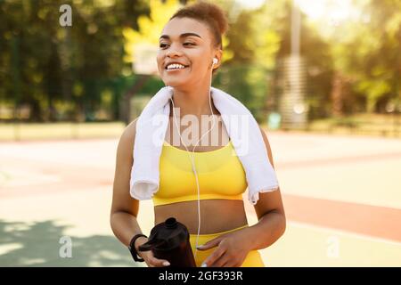 Lächelnde schwarze Frau in gelber Sportkleidung, die Musik hört Stockfoto