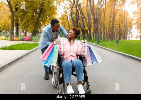 Liebevolles, tausendjähriges behinderten Paar mit Geschenktüten, das im Herbst zusammen aus dem Verkauf im Geschäft nach Hause zurückkehrt Stockfoto