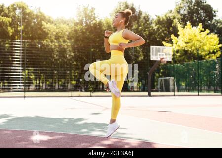 Sportliche schwarze Frau in gelber Sportswear springen und laufen Stockfoto
