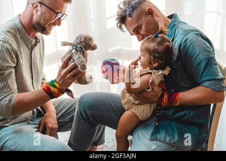 Schwule Männer mit adoptierten Mädchen zu Hause - zwei gutaussehende Väter spielen mit ihrer Tochter - LGBTQ+ Familie zu Hause - Diversity-Konzept und LGBT Stockfoto