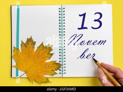 Tag des 13. november. Handschriftlich das Datum 13. november in einem offenen Notizbuch mit einem schönen natürlichen Ahornblatt auf gelbem Hintergrund. Herbstmonat, Stockfoto