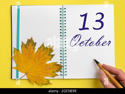 Tag des 13. oktober. Handschriftlich das Datum 13. oktober in einem offenen Notizbuch mit einem schönen natürlichen Ahornblatt auf gelbem Hintergrund. Herbstmonat, da Stockfoto