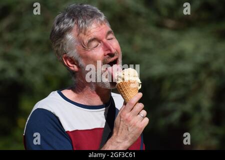 Ein britischer grauhaariger Mann mittleren Alters in den Fünfzigern, der einen Eiskegel isst Stockfoto