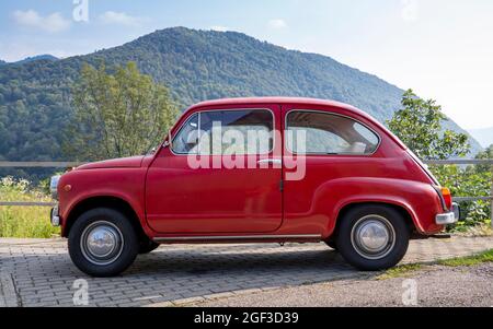 Fiat 600, kleines rotes italienisches Oldtimer, das auf einer Bergstraße geparkt ist Stockfoto