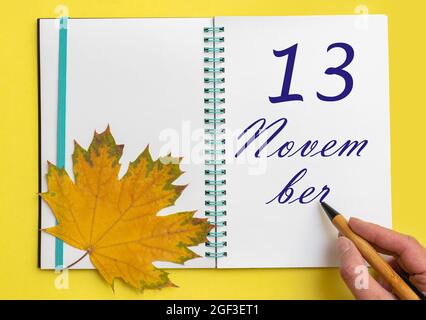 Tag des 13. november. Handschriftlich das Datum 13. november in einem offenen Notizbuch mit einem schönen natürlichen Ahornblatt auf gelbem Hintergrund. Herbstmonat, Stockfoto
