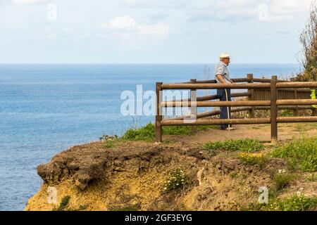 Lastres, Spanien. Ein alter Mann mit Hut und Stock ruht in der Nähe des Leuchtturms von Luces im Atlantischen Ozean in Asturien Stockfoto